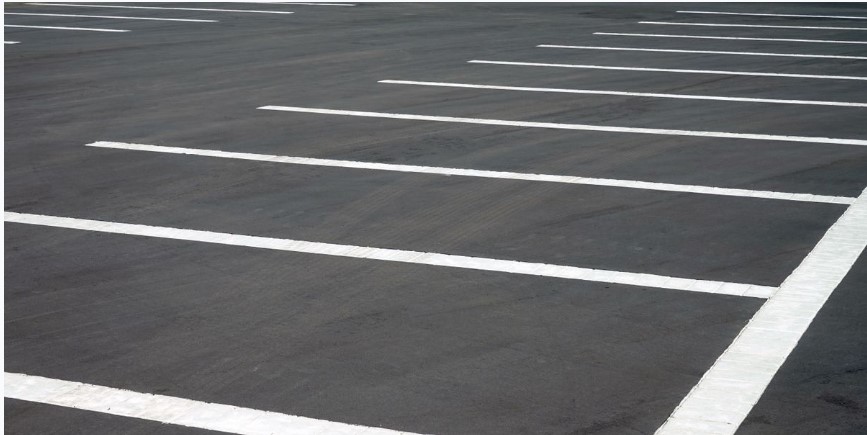 Empty paved parking lot with white painted space lines marking parking spots.