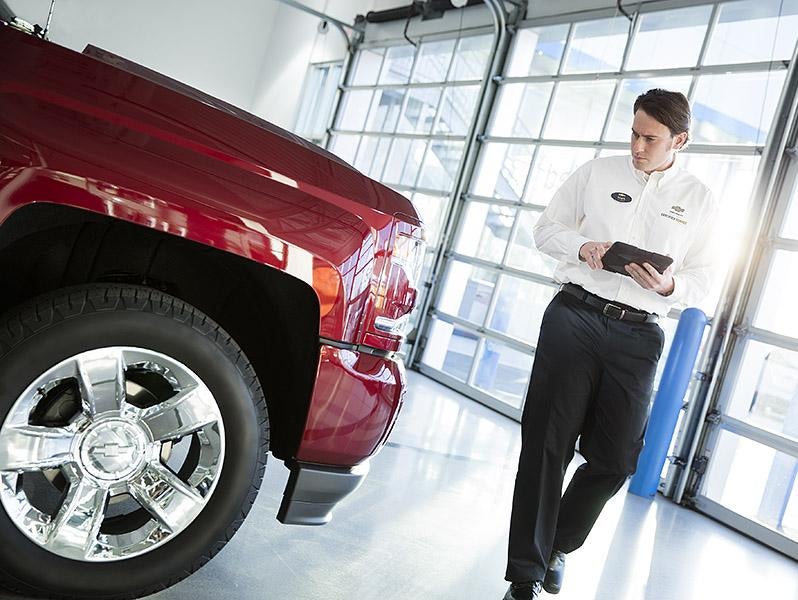 Chevrolet technician inspecting a red pickup truck in a service center using a digital tablet.