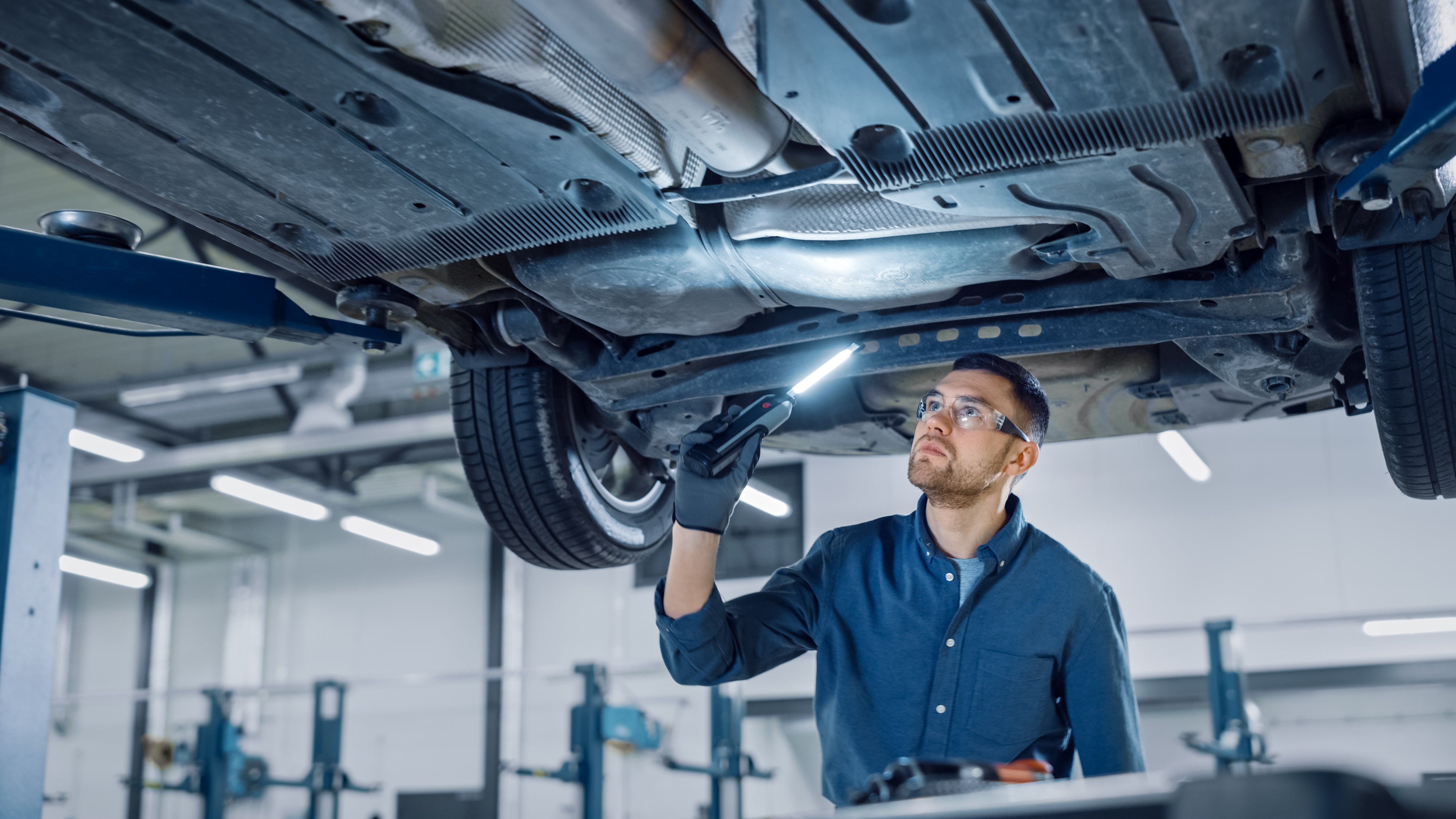 Automotive technician inspecting a vehicle's undercarriage on a lift during service.